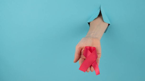 A womans hand with a red bow sticks out of a hole in a blue background. Breast cancer symbol - Φωτογραφία, εικόνα
