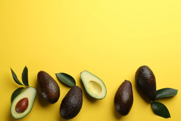 Whole and cut ripe avocadoes with green leaves on yellow background, flat lay. Space for text - Foto, Imagem