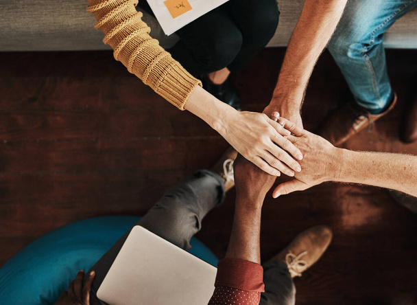 Lets pull together and make great things happen. High angle shot of a group of unrecognizable businesspeople joining their hands together in a huddle - Foto, imagen