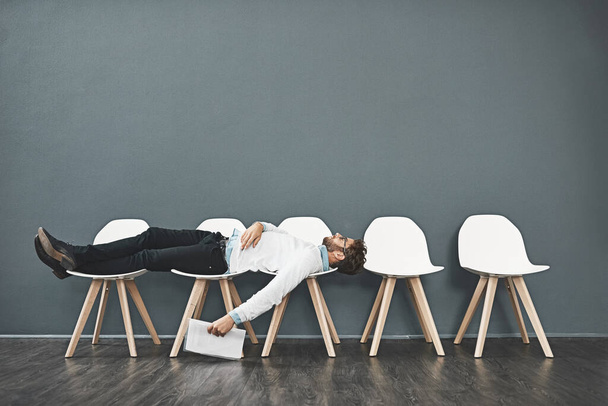 Can this wait get any longer. a young man lying down on a row of chairs while waiting in line for a job interview - 写真・画像