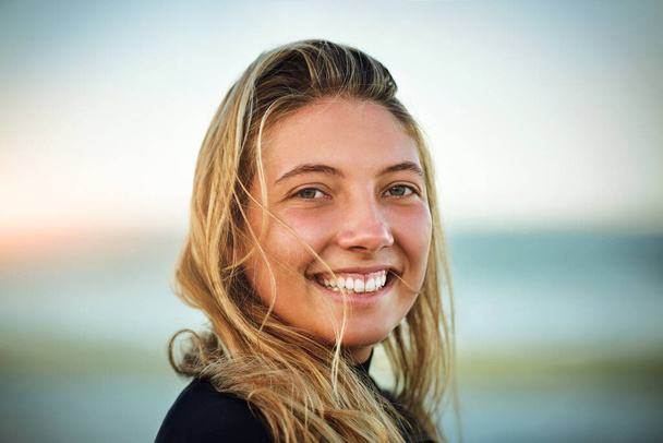 Ο θαλασσινός αέρας με κάνει να χαμογελάω. Καλλιεργημένη προσωπογραφία ενός ελκυστικού νεαρού θηλυκού σέρφερ που στέκεται στην παραλία - Φωτογραφία, εικόνα