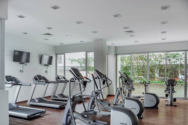 gym as an amenity within apartment towers, treadmill with televisions, exercise and ecliptic bikes, wood floors and white ceilings. A line of empty treadmills in a private gym for building residents. - Photo, Image