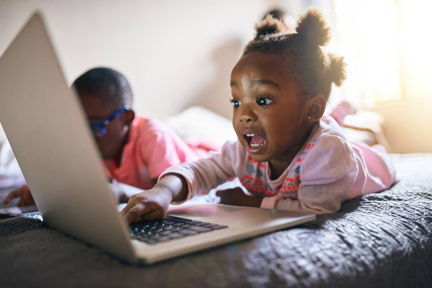 Shes a bundle of excitement. an adorable little girl playing on a laptop next to her brother at home - Photo, image