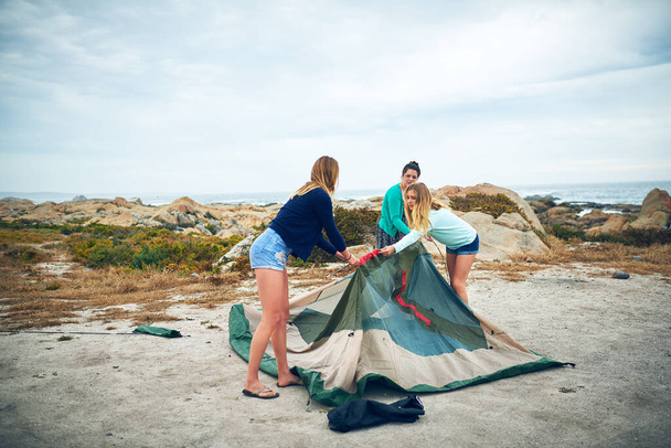 We all pitch in to set up the tent. a group of female friends setting up a tent outdoors - Photo, image