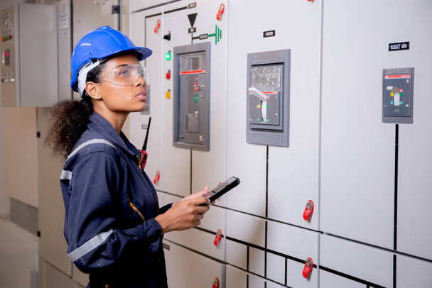 Electrical young asian woman engineer examining maintenance cabinet system electric and using tablet in control room at industrial factory, technician or electrician inspection power distribution. - Fotó, kép