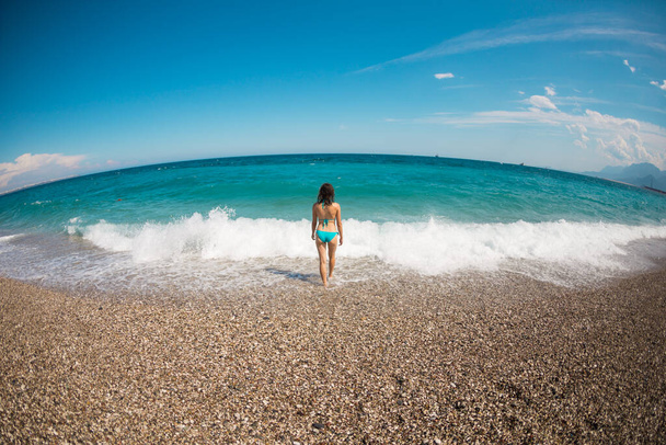 Жінка йде вздовж берега в Анталії, дівчина в купальнику відпочиває на узбережжі моря, морські хвилі і блакитне небо, жінка купається на пляжі.. - Фото, зображення