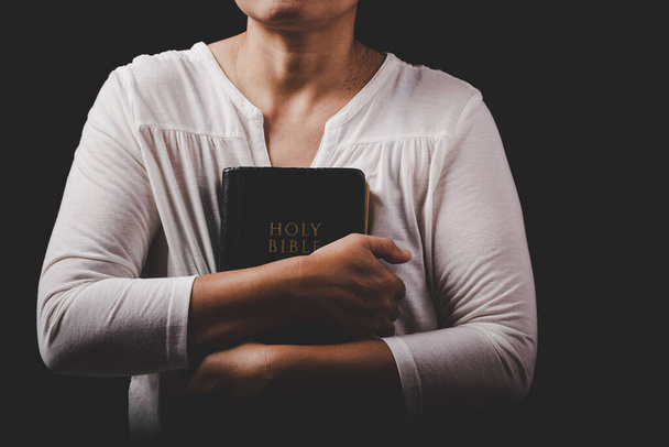 christian woman hand on holy bible are pray and worship for thank god in church with black background, adult female person are reading book, concept for faith, spirituality and religion - Foto, afbeelding