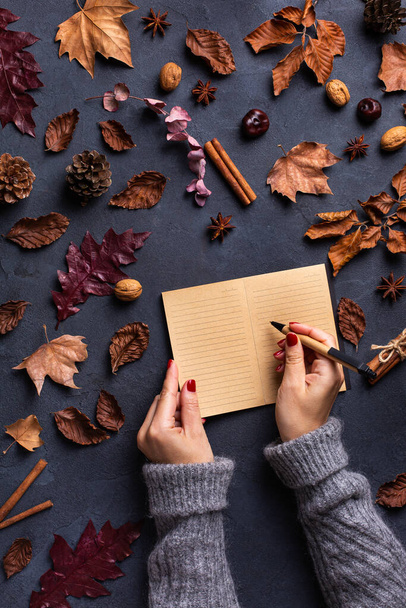 Autumn fall thanksgiving day composition with decorative dried leaves. Female hands writing in notebook. Flat lay, view from above, still life seasonal background for greeting card, copy space - Foto, immagini
