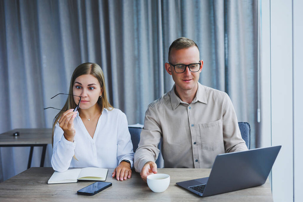 Young business team, male and female colleagues talking at work, discussing a new project with a laptop, young executives having a friendly conversation, collaborating in teamwork in the office - Foto, Bild