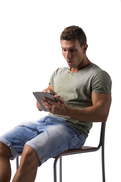 Muscular young man sitting on chair while reading from e-book device - Foto, afbeelding
