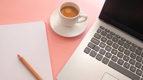 Blank page of a notebook next to a laptop and a white cup with coffee on a light pink background - 写真・画像