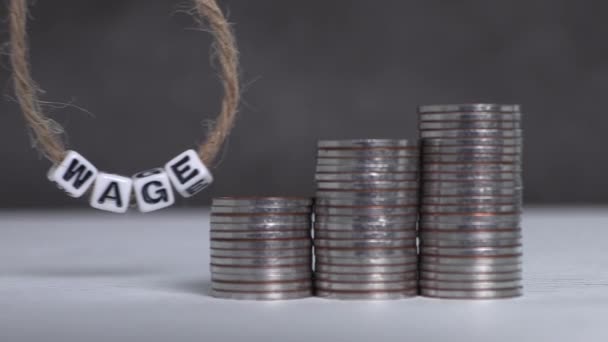 Three piles of graph-shaped coins and a WAGE text on white cube swinging on a string. Business concept with piles of coins and text. - Video