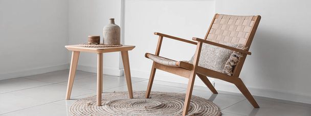 Стильне плетене крісло з дерев'яним столом і вазою біля світлої стіни в кімнаті
 - Фото, зображення