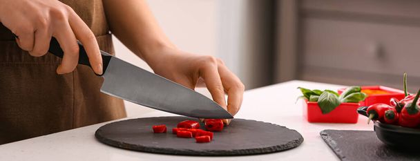 Woman with knife cutting hot chili pepper in kitchen - Zdjęcie, obraz