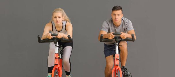 Young people training on exercise bikes against grey background - 写真・画像