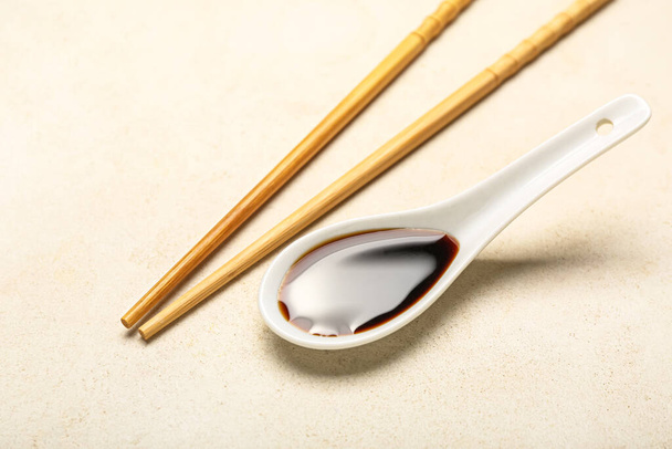 Spoon of soy sauce and chopsticks on light background - Photo, Image