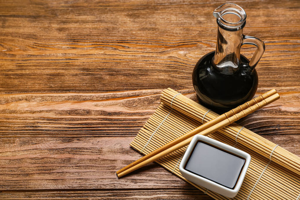 Bowl and jug of soy sauce, chopsticks with bamboo mat on wooden background - Valokuva, kuva