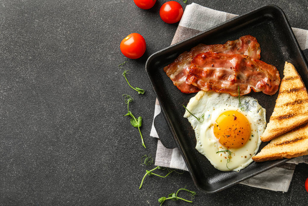Composition with frying pan of tasty fried egg, bacon, toasts and tomatoes on dark background - Foto, immagini