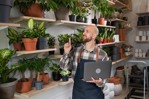 Handsome Caucasian man holding his laptop while working on his own floral shop in front of the camera he smiling large happy concept of entrepreneur and small business. Portrait - Photo, Image