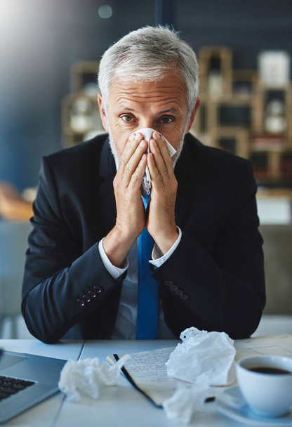 Maybe it will be over before I know. a frustrated businessman using a tissue to sneeze in while being seated in the office - Photo, Image