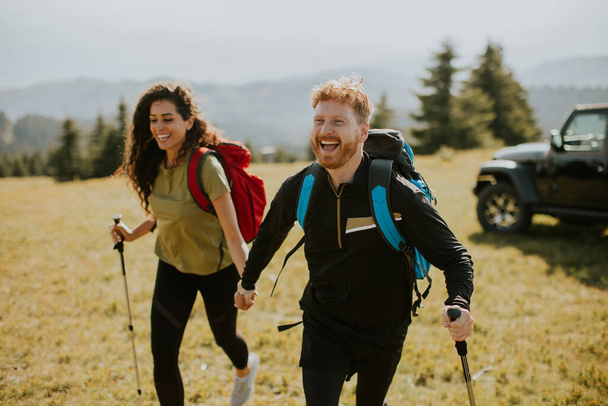 Lächelndes junges Paar läuft mit Rucksack über grüne Hügel - Foto, Bild