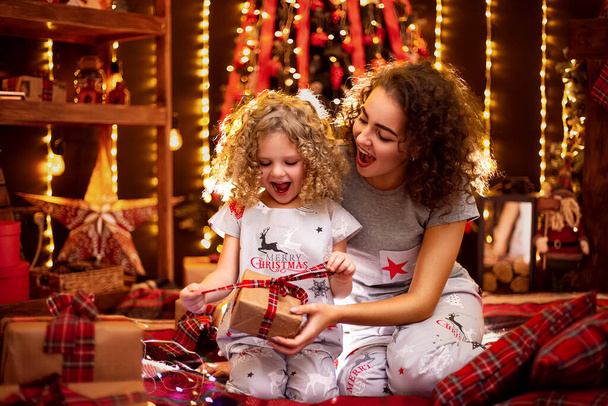 Cheerful cute curly little girl and her older sister exchanging gifts. Sisters having fun near christmas tree indoors. Loving family with presents in christmas room.  - Foto, imagen