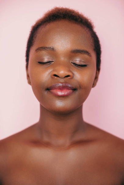 Front view of an African American woman smiling with closed eyes posing on pink background representing spa service. Attractive beautiful girl. Young woman face - Foto, Bild