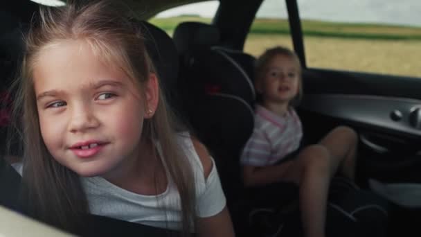 Καυκάσιος κορίτσι 8 ετών κοιτάζει έξω από το παράθυρο του αυτοκινήτου, ενώ το ταξίδι με το αυτοκίνητο και την αδελφή της στο παρασκήνιο. Πυροβολήθηκε με κόκκινη κάμερα ηλίου σε 8K. - Πλάνα, βίντεο