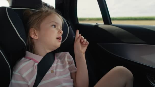 Caucasian girl of 6 years sitting in safety seat and looking out of the car window while car trip. Shot with RED helium camera in 8K. - Footage, Video