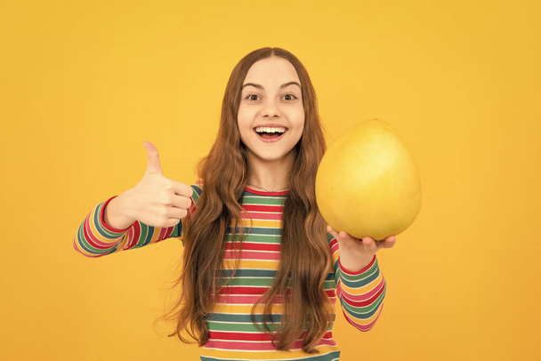 Letní ovoce. Teenager dítě dívka držet citrusové plody pummelo nebo pomelo, izolované na žlutém pozadí. Zdravé stravování dětí - Fotografie, Obrázek