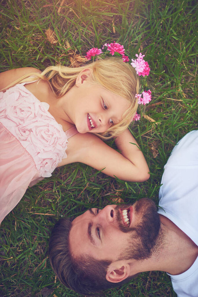 We always have the best of times together. a happy daughter and father lying on the ground looking at one another outside in nature - Foto, Bild
