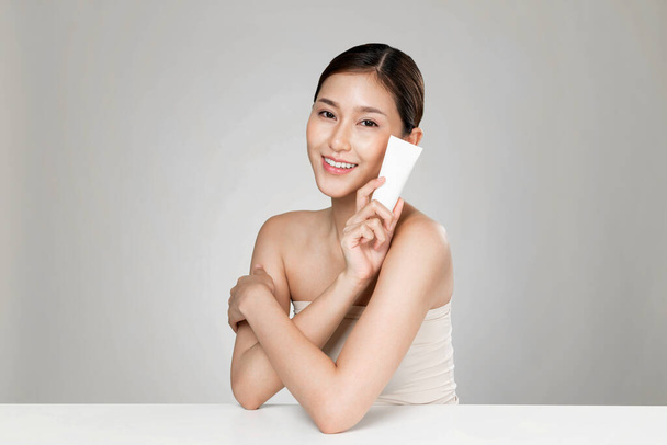 Ardent woman smiling holding mockup product for advertising text place, light grey background. Concept of healthcare for skin, beauty care product for advertising. - Foto, immagini