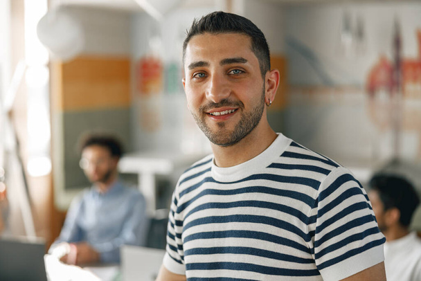 Smiling businessman in casual clothes standing in modern office on colleagues background - Foto, afbeelding