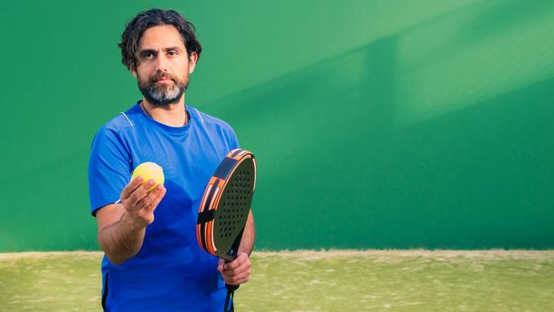Monitor of padel holding black racket with yellow tennis ball in the hand. Class to student on outdoor tennis court. Man paddel player playing a match in the open - Photo, Image