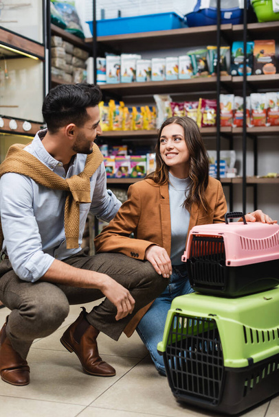 Positive interracial couple talking near animal cages in pet shop  - Valokuva, kuva