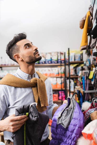 Arabian man holding animal jackets in pet shop  - Foto, immagini