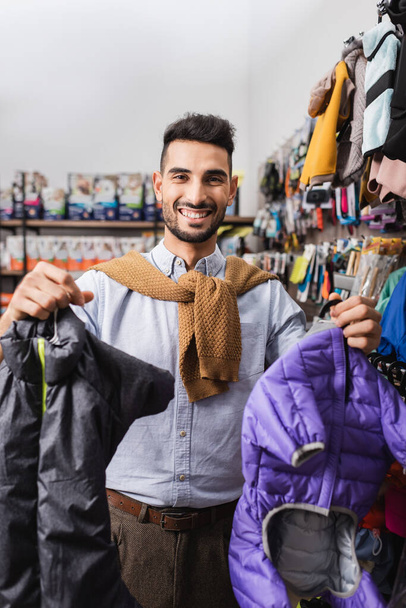 Positive muslim man holding animal jackets in pet shop - Фото, изображение