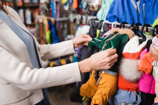 Cropped view of woman choosing animal jackets in blurred pet shop  - Foto, imagen