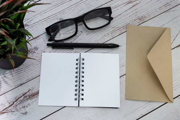 Notepad with brown envelop, reading glasses, pen and potted plant on wooden desk. Flat lay. Copy space. - Valokuva, kuva
