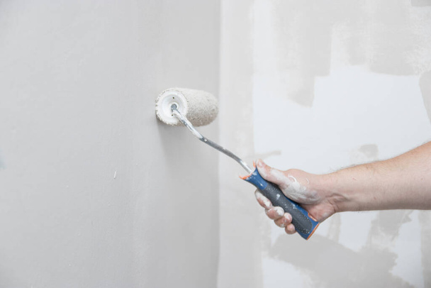 Man with roller painting wall. Close up of house paint roller. Home repairs with family. Update, improvement living room. - Foto, immagini