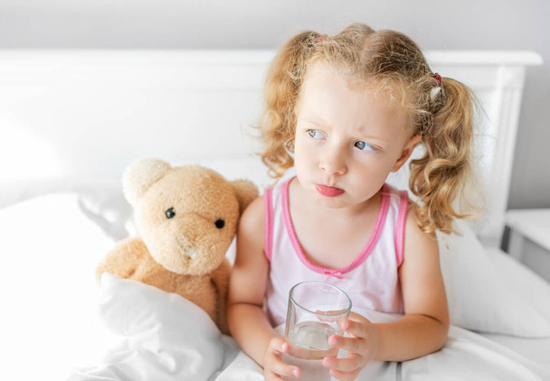 The child drinks water in bed. Drinking regimen during illness. - Photo, image