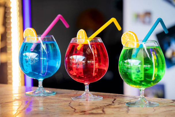 Three colorful bright cocktails with a straw and a slice of lemon. Chemical composition and unhealthy alcohol - Fotoğraf, Görsel