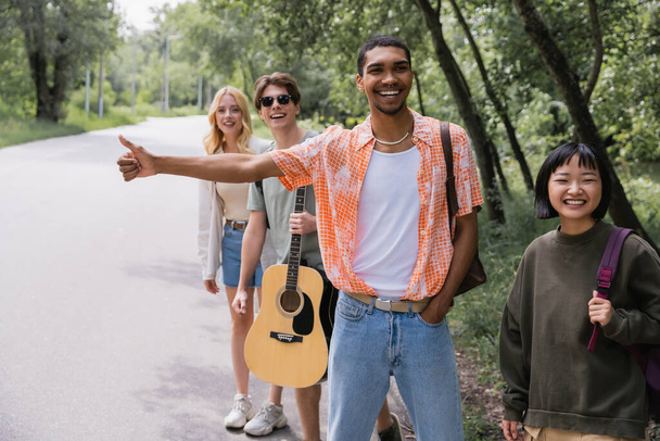 cheerful interracial hitchhikers stopping car on countryside road - Photo, image