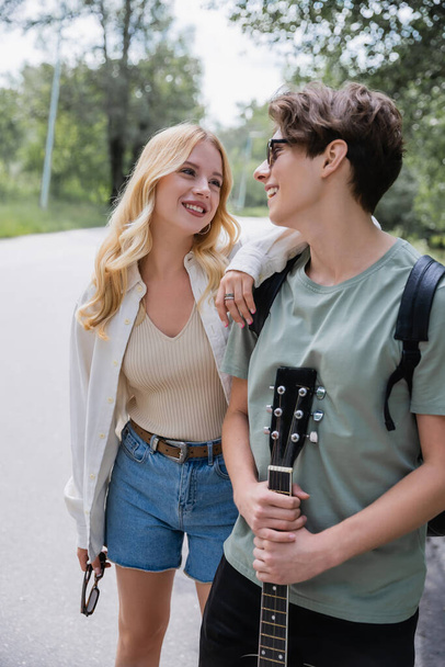 man with guitar and blonde woman smiling at each other while walking in countryside - Photo, image