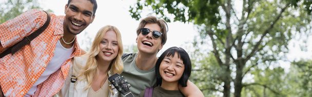 young and cheerful multicultural travelers looking at camera outdoors, banner - Foto, afbeelding