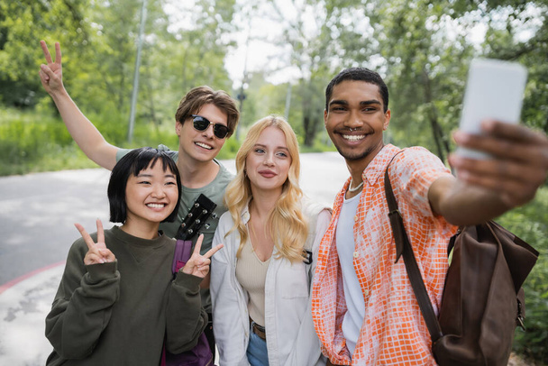 happy african american man taking selfie with interracial friends showing victory signs - Photo, Image
