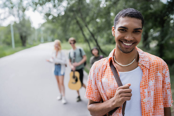 young african american man smiling at camera near blurred travelers - Foto, imagen