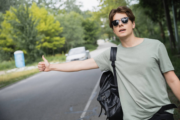 young hitchhiker in sunglasses stopping car on countryside road - Fotografie, Obrázek