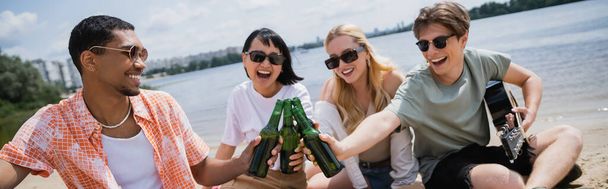 χαρούμενα διαφυλετικοί φίλοι σε γυαλιά ηλίου τσούξιμο μπουκάλια κατά τη διάρκεια πάρτι μπύρα, πανό - Φωτογραφία, εικόνα