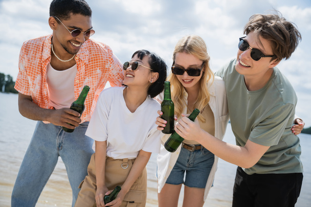 joyful multiethnic friends holding beer bottles on beach - Valokuva, kuva